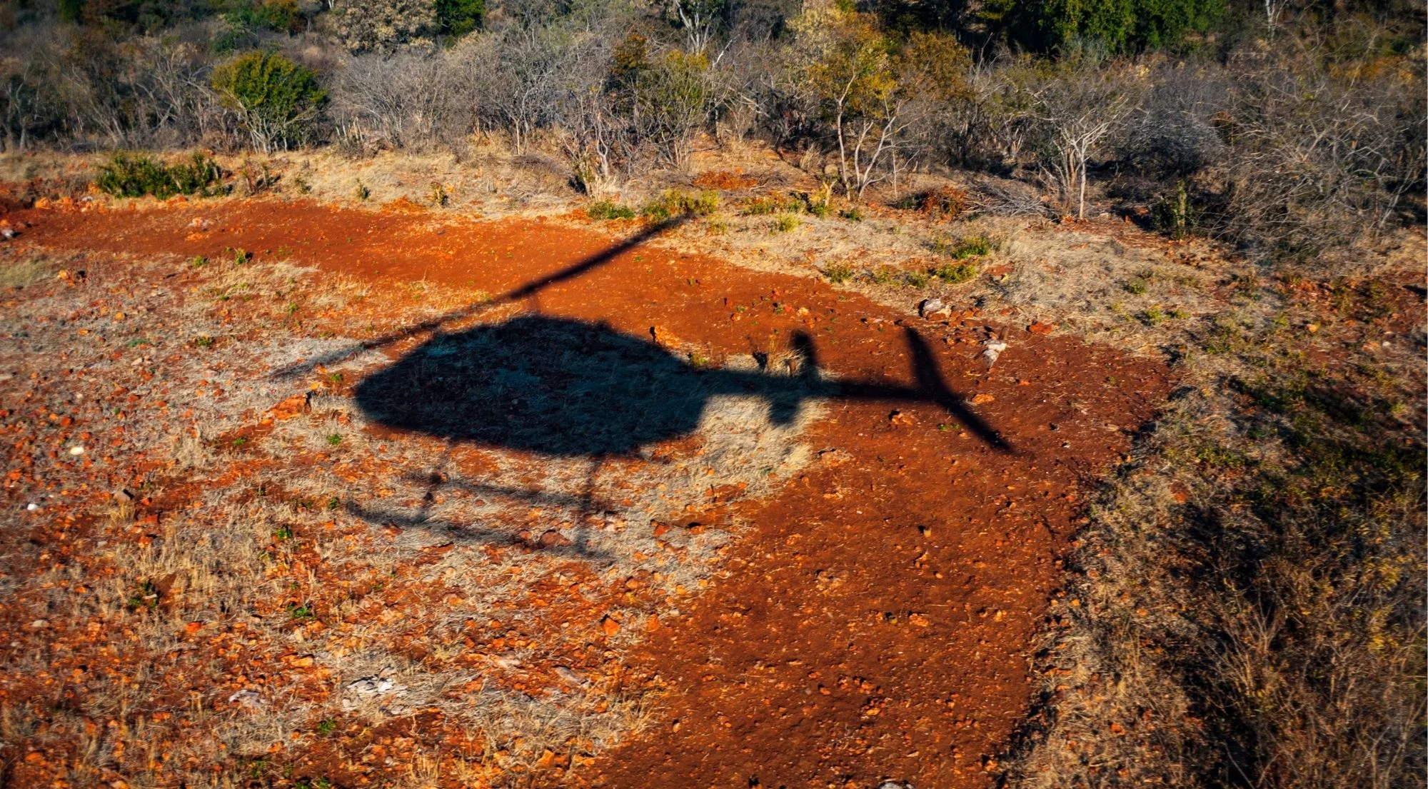 Shadow of a helicopter cast over the red African soil of Zimbabwe during a scenic flight over Victoria Falls