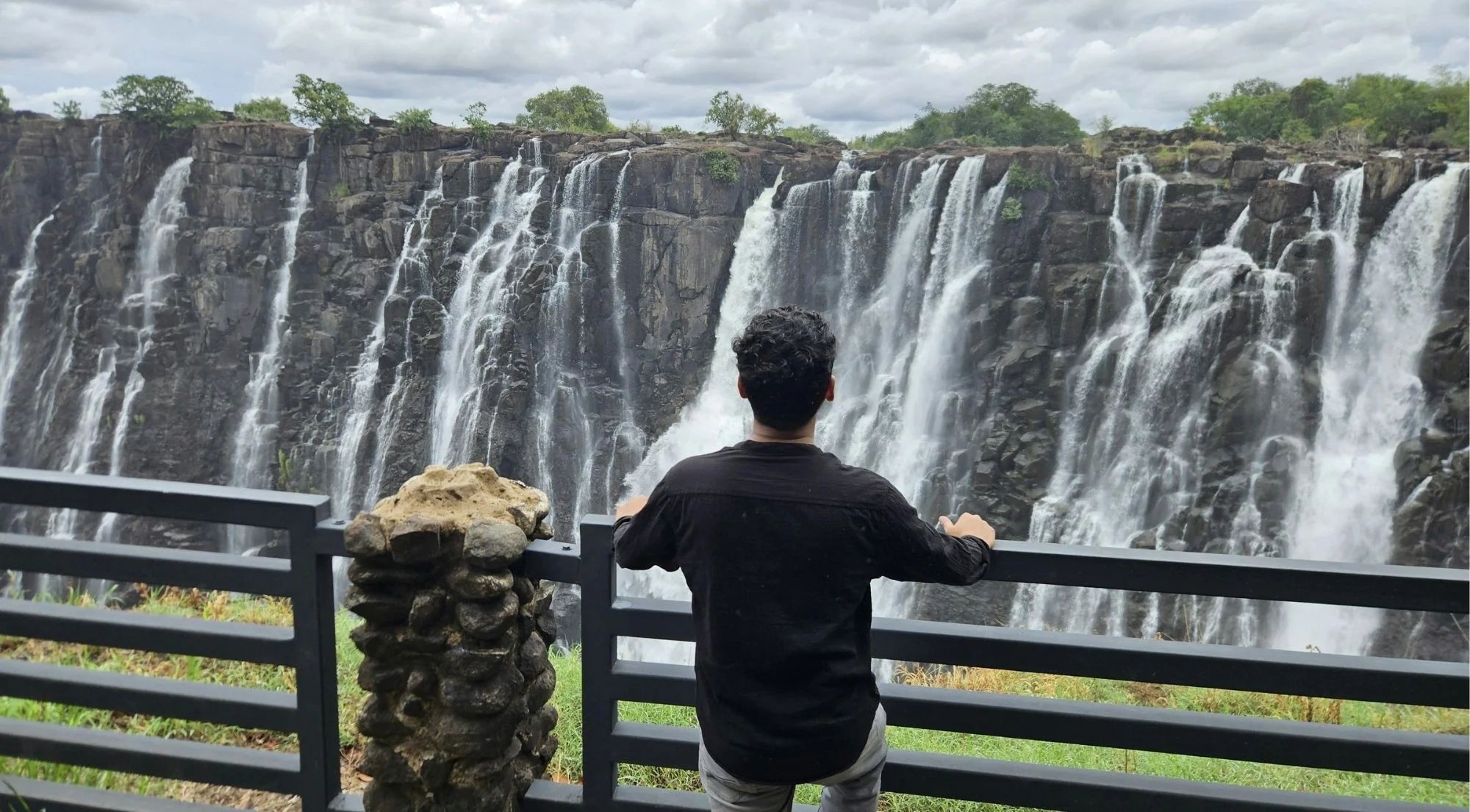 Traveller at a viewing platform overlooking the full width of Victoria Falls, surrounded by lush Zimbabwean rainforest